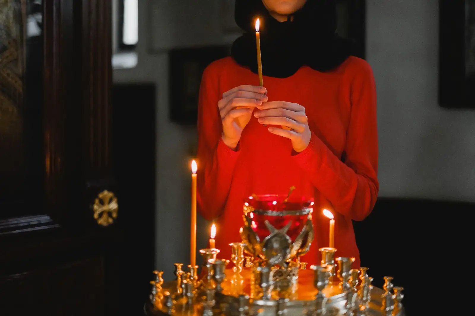 A woman in prayer holding a candle in a dimly lit church, reflecting spirituality.